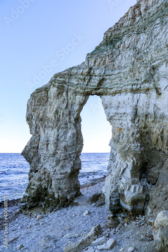 rocky stone arch from various natural rocks, on river bank. layered hollow stone arch on pebble beach near river. unusual rock in form of arch or gate of great height on the coast.