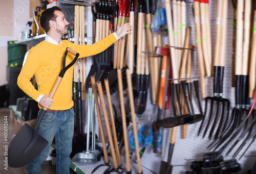 Adult guy deciding on best shovel in garden equipment shop