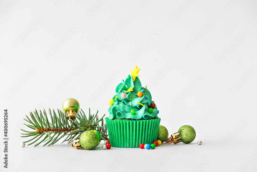 Tasty Christmas cupcake and decor on light background
