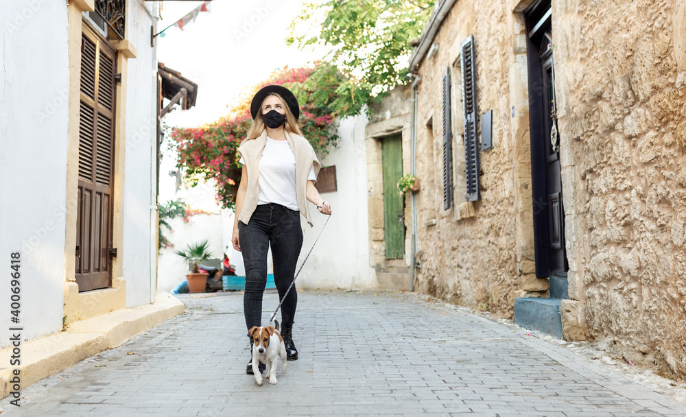 tourist in protective mask holds dog on hands and walking in old city Coronavirus disease COVID-19 new travel reality. Girl in medical mask walking. Coronavirus pandemic Precautions. Travel with pets tourist in protective mask holds dog on hands and walking in old city Coronavirus disease COVID-19 new travel reality. Girl in medical mask walking. Coronavirus pandemic Precautions. Travel with pets