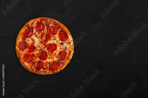 Tasty pizza with salame on dark concrete surface with place for your text. Top view of sliced pizza. 