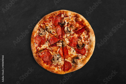 Tasty pizza with salame and mushrooms on dark concrete surface. Top view of sliced pizza. 