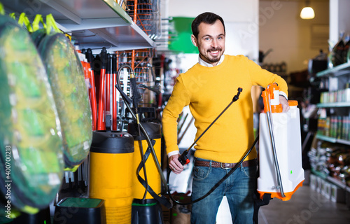 Young cheerful man choosing garden sprayer in garden equipment shop