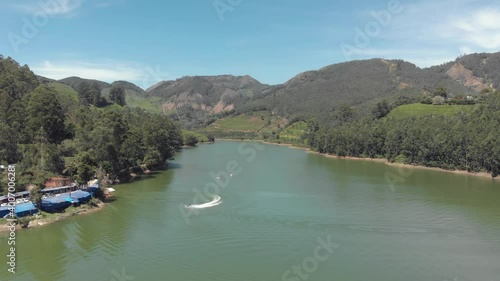 Jet skiing on the shore of Mattupetty Lake near Munnar, overlooked by mountainous landscape in India - Aerial Low angle Panoramic shot photo