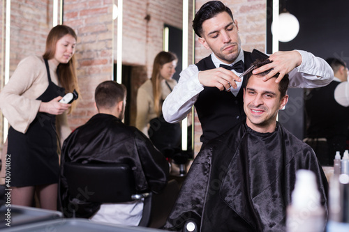 Skillful man barber making haircutting for male client in hair studio