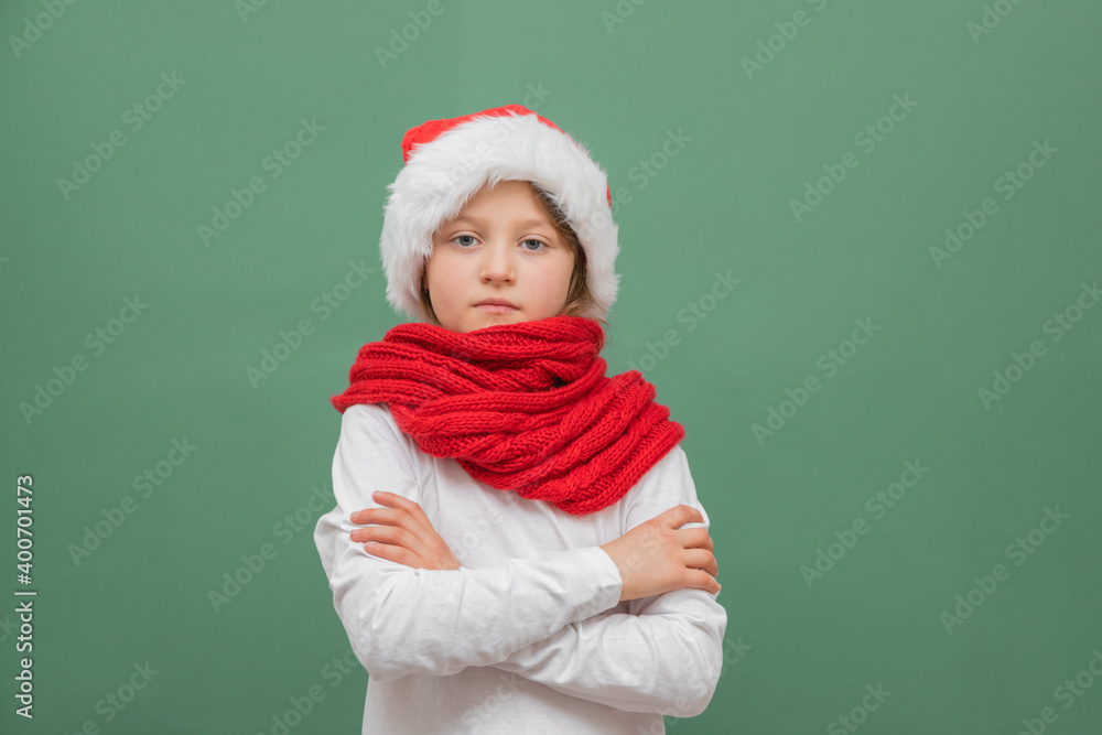 Happy new year and merry christmas. Cute little caucasian girl in a santa hat and a red scarf on a green background with place for text. Happy new year and merry christmas. Cute little caucasian girl in a santa hat and a red scarf on a green background with place for text.