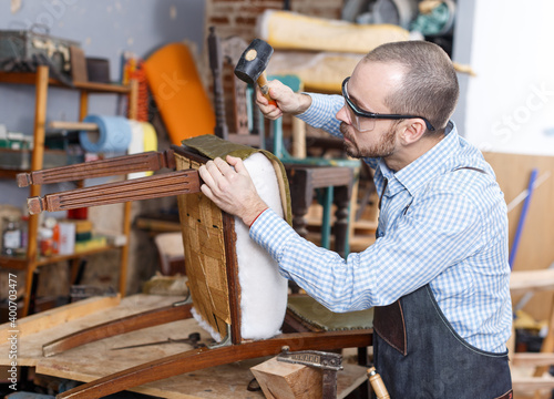 Qualified workman upholstering chair in repair furniture workshop