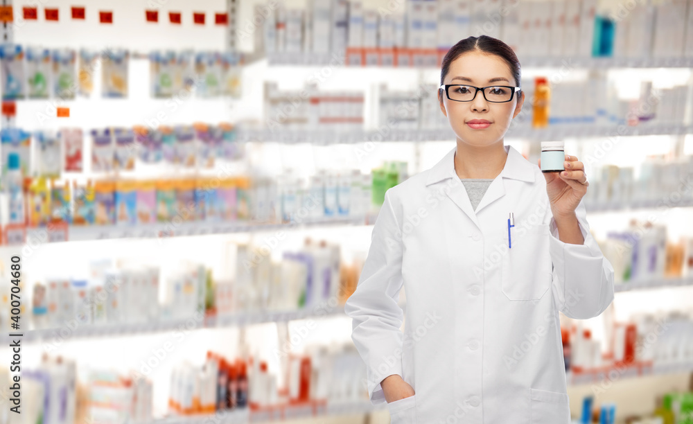 medicine, profession and healthcare concept - asian female pharmacist or doctor holding jar of pills over pharmacy background