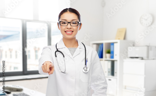 medicine  profession and healthcare concept - happy smiling asian female doctor or nurse with stethoscope pointing to camera over hospital background