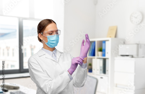 science, health and medicine concept - young female doctor or scientist wearing gloves, goggles and face protective medical mask for protection from virus over hospital background