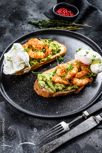 Sandwich topped with fresh prawns, shrimps on avocado with egg. A healthy food, Scandinavian cuisine. Black background. Top view