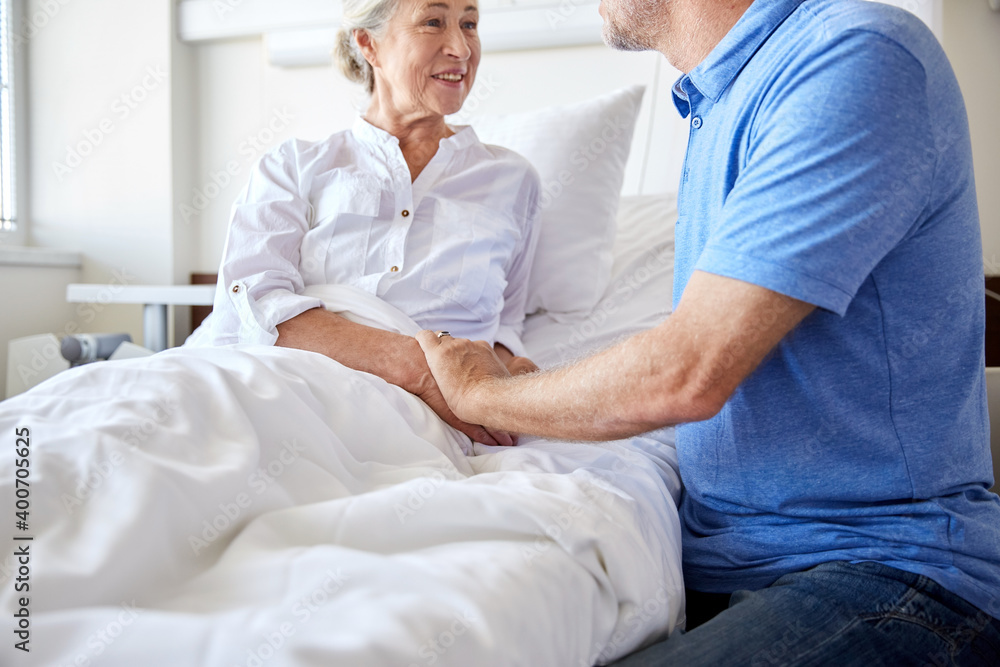 medicine, healthcare and people concept - happy senior man visiting and cheering his woman lying in bed at hospital ward medicine, healthcare and people concept - happy senior man visiting and cheering his woman lying in bed at hospital ward