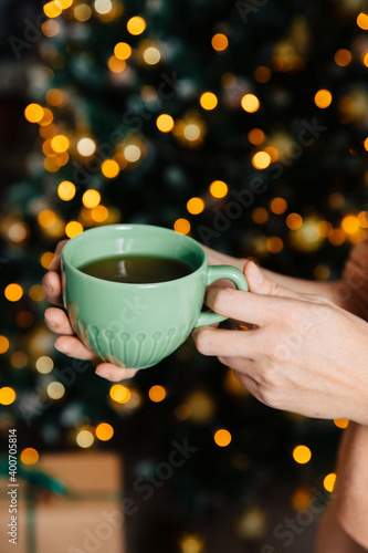 a green cup of tea held in his hand on the background of a decorated Christmas tree