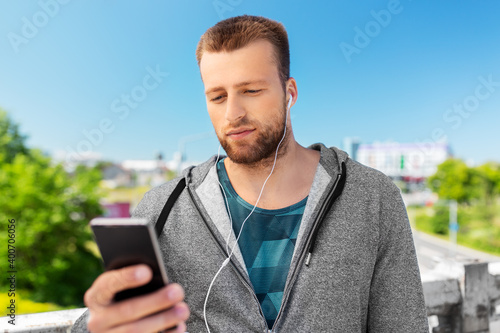 fitness, sport and technology concept - young man with earphones and smartphone listening to music outdoors