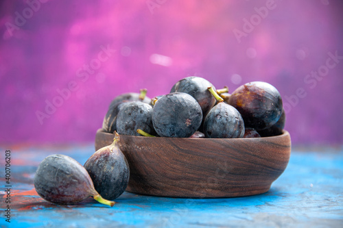 Side view of black mission figs inside and outside of a small brown pot on blue table and on pink background photo