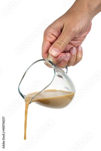Hand holding a transparent glass and pouring coffee with cream, isolated on a white background