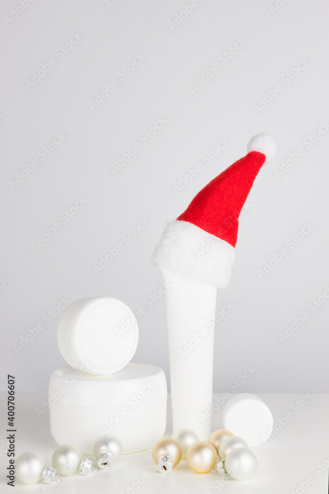 New Year's cosmetic concept. White jars of cream and tubes on a white table with a santa hat. Vertical orientation. Place for text New Year's cosmetic concept. White jars of cream and tubes on a white table with a santa hat. Vertical orientation. Place for text