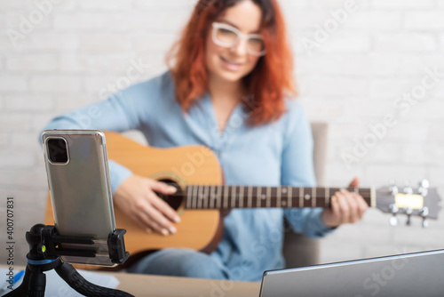 An attractive red-haired woman blogs on music. The girl sings, plays the guitar and records video on a smartphone