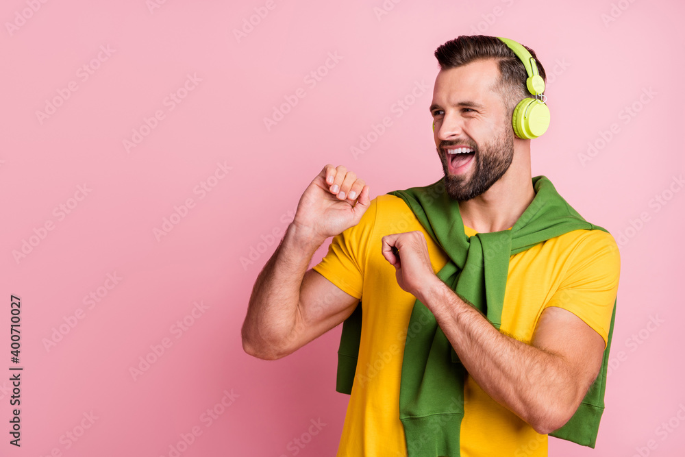 Photo attractive young man dance empty space raise fists wear headphones isolated on pink color background Photo attractive young man dance empty space raise fists wear headphones isolated on pink color background
