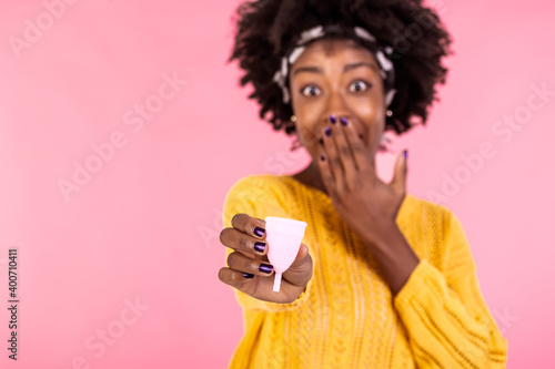 Serious dark skinned woman holds bell shaped menstruation cup for inserting in vagina, trapping menstrual fluid and leakage protection, tells secret information and tips how to use it, makes hush sign