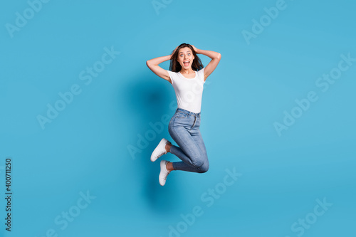 Full length photo of attractive surprised woman hold hands head jump up isolated on blue color background © deagreez