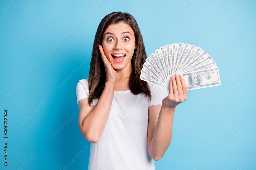 Photo of young shocked happy smiling amazed lovely girl with money hold hand cheek isolated on blue color background Photo of young shocked happy smiling amazed lovely girl with money hold hand cheek isolated on blue color background