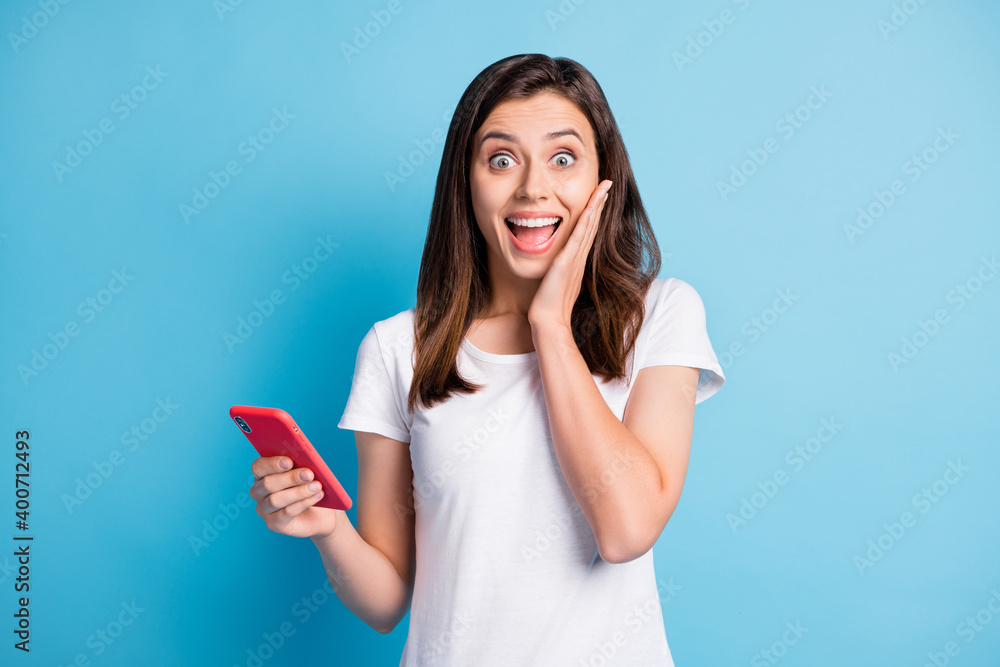 Naklejka premium Photo of young happy shocked amazed crazy girl hold smartphone sees unbelievable news isolated on blue color background
