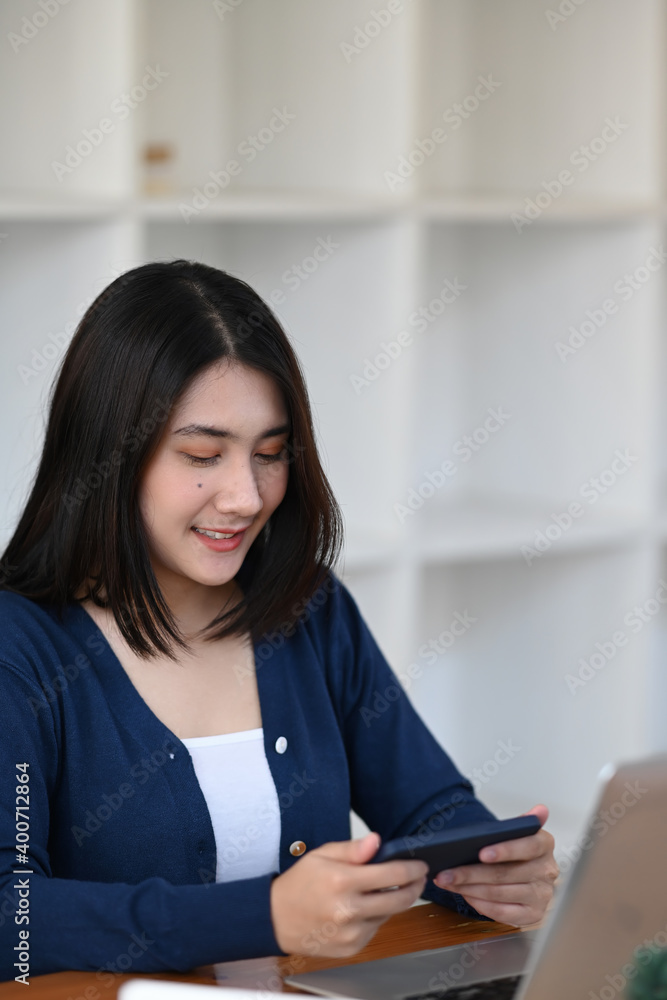 A happy young woman enjoy playing game application on mobile phone while sitting in front of her computer laptop. A happy young woman enjoy playing game application on mobile phone while sitting in front of her computer laptop.