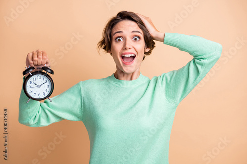 Photo of young attractive girl amazed shocked surprised crazy hold clock hand touch head isolated over beige color background