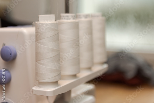 Detail of four thread spools with white thread on overlock sewing machine