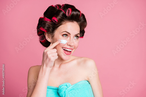 Close-up portrait of nice cheerful housewife applying cream on cheek anti age wrinkles rejuvenation isolated over pink color background
