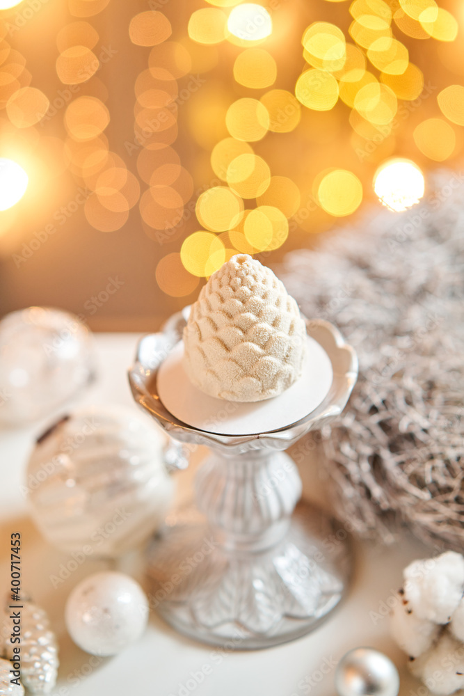 Dessert in the form of Christmas pine cone. Mini mousse pastry dessert covered with velour. Garland lamps bokeh on background. Modern european cake. French cuisine. Christmas theme. Copy space