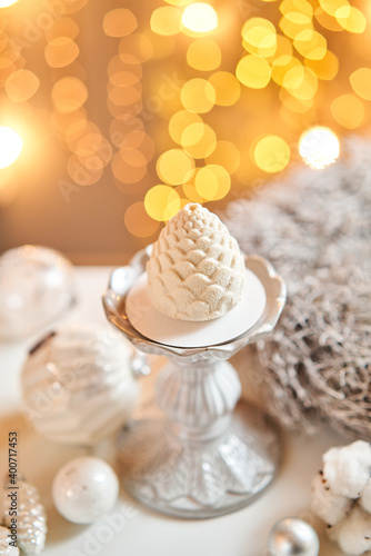 Dessert in the form of Christmas pine cone. Mini mousse pastry dessert covered with velour. Garland lamps bokeh on background. Modern european cake. French cuisine. Christmas theme. Copy space