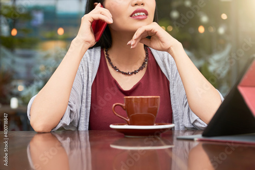 Cropped image of pretty young woman drinking coffee in caffeteria and talking on phone photo