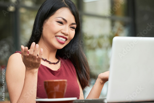 Cheerful beautiful young business lady video calling her colleague or family memeber when sitting at table in outdoor cafe photo