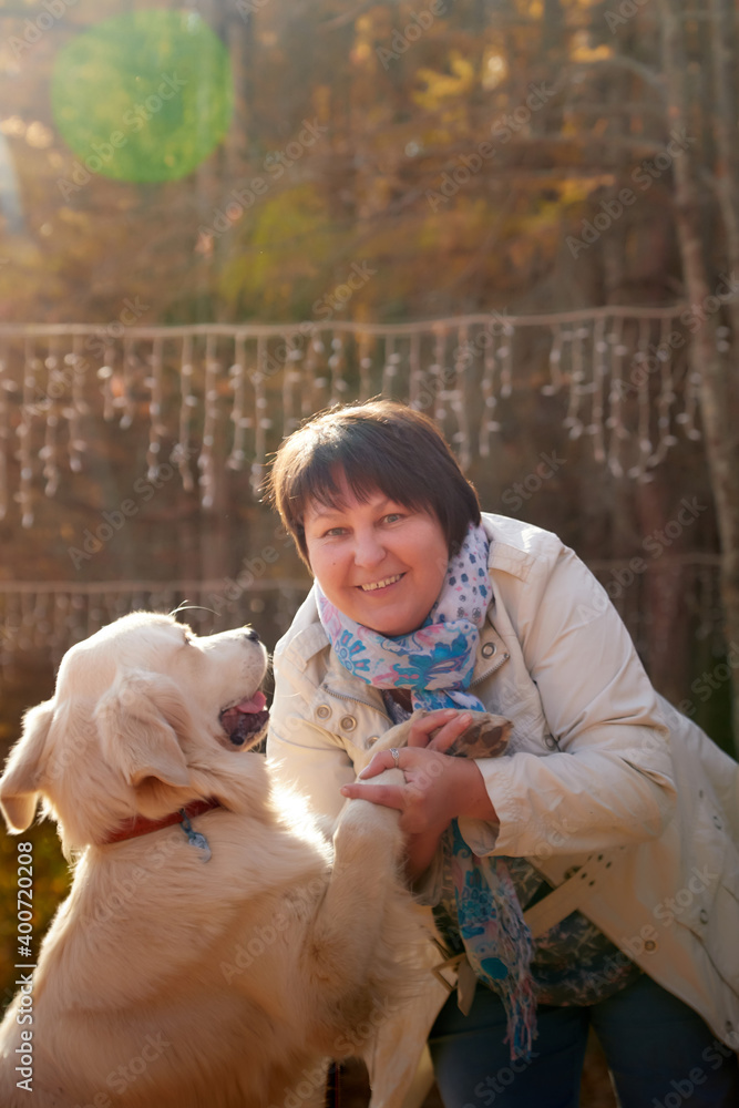 A plump woman with a white Labrador dog walking in a Park or forest on a Sunny autumn day. A plump woman with a white Labrador dog walking in a Park or forest on a Sunny autumn day.
