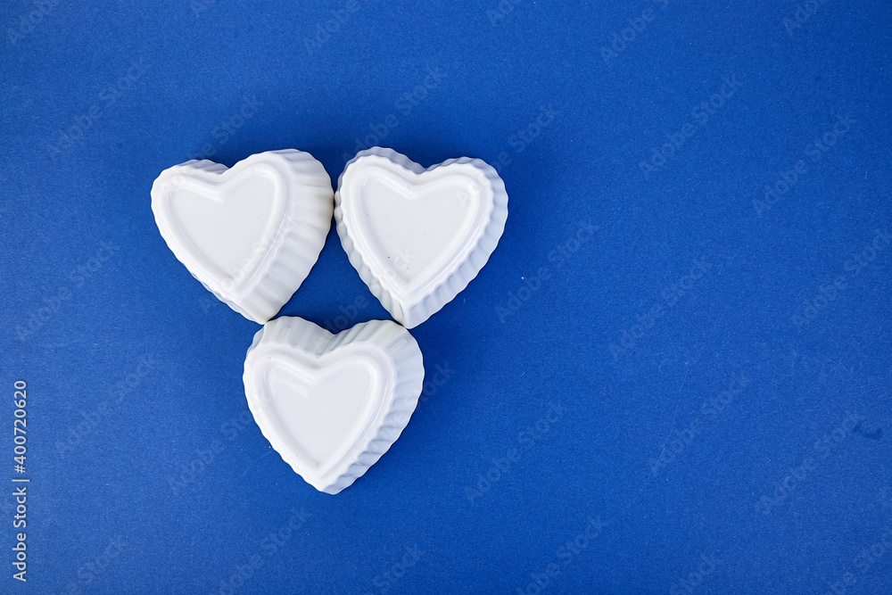 Fototapeta premium White ceramic hearts on blue trend color background.