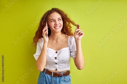 attractive young girl in blouse talk on phone with girlfriend, curly female enjoy sharing news with someone, isolated over green background in studio