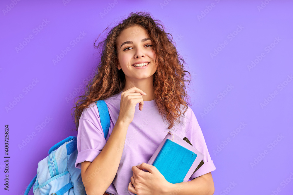 young beautiful school girl with curly hair keen on studying, preparing for school or college, isolated purple background young beautiful school girl with curly hair keen on studying, preparing for school or college, isolated purple background