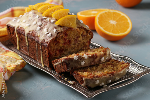 Homemade orange cake with cranberry covered with icing and slices oranges on metal tray on a light blue background. Closeup. Horizontal format