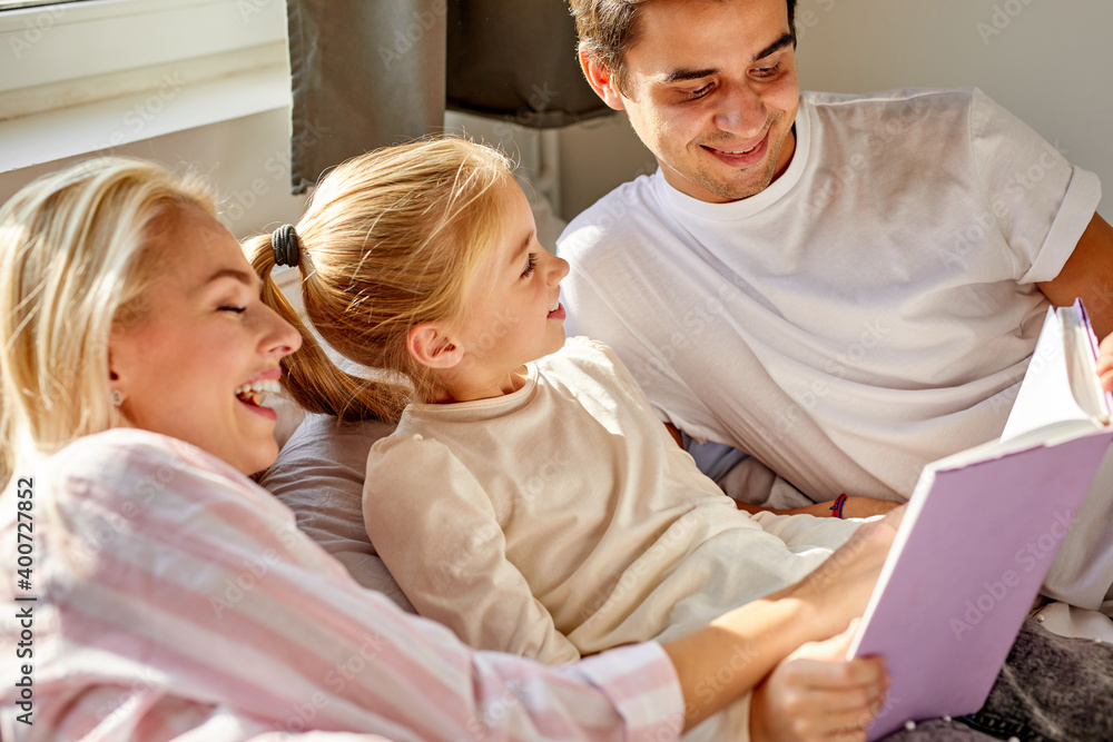 optimistic parents read book with child on bed before going to sleep, have talk, discuss the tale optimistic parents read book with child on bed before going to sleep, have talk, discuss the tale
