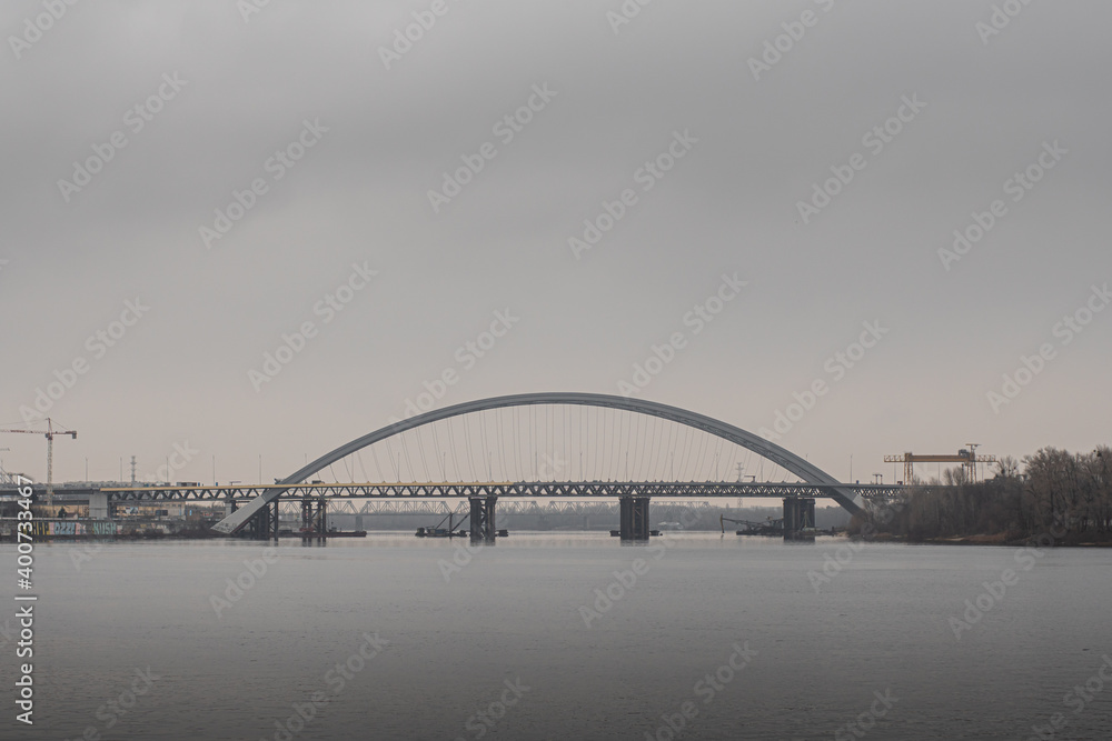 Arch bridge on Podil over the river Dnieper in the city of Kiev, on a cloudy day in autumn, at the last stage of construction, side view.