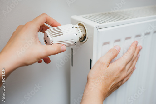 Close up shot of Caucasian female's hand adjusting radiator temperature using thermostat. Home with central heating. photo
