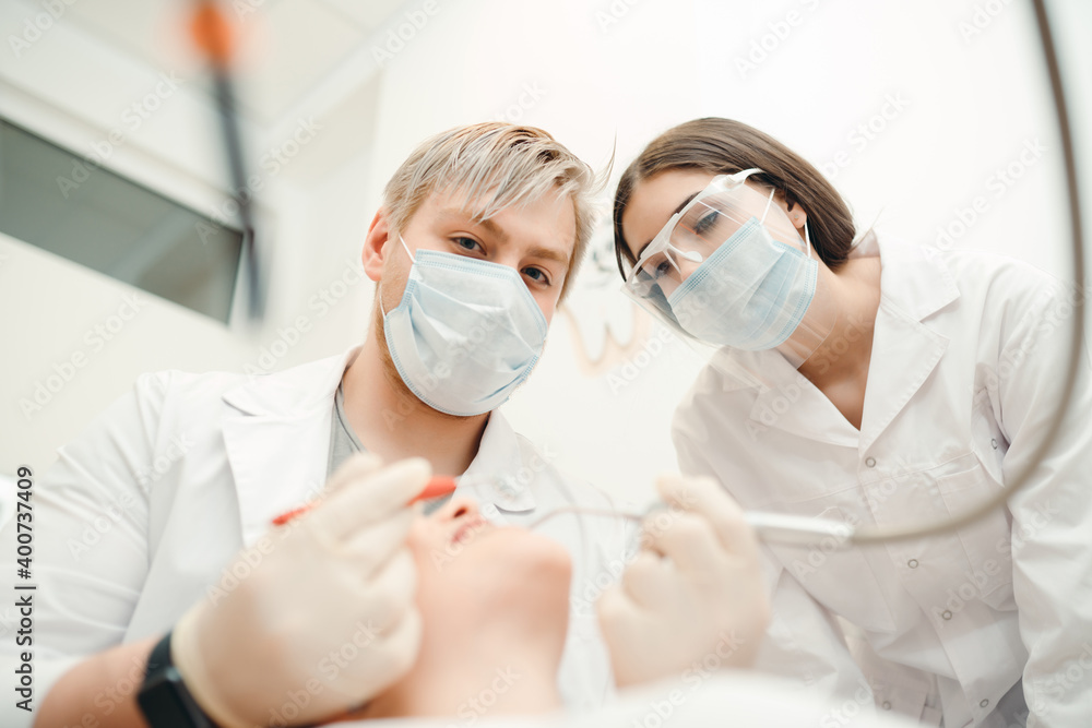 The doctor performs the dental treatment procedure for the client while the assistant looks at it
