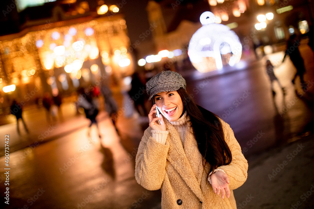 Pretty young woman using her mobile phone in the street at Christmas time
