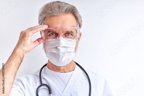 doctor man wearing protective eyeglasses for preparing for work, elderly male in white medical suit looks at camera isolated on white background