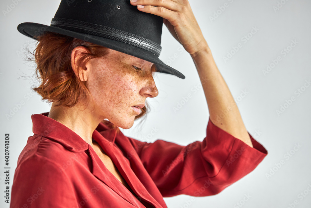 woman with short natural red haired in elegant black hat looking down, having charming appearance and personality. side view