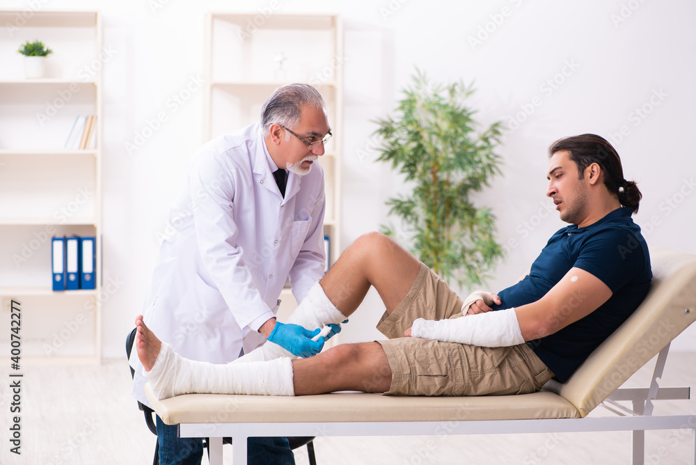 Fototapeta premium Young injured man visiting old doctor traumatologist