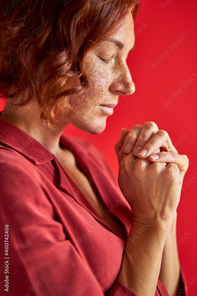 female dreams about something holding hands together and keeping eyes closed, redhead lady thinks. isolated over red background