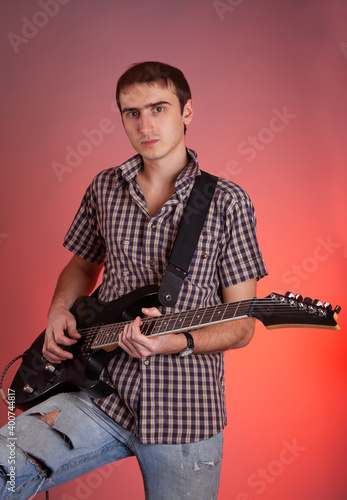 Expressive young man playing guitar on red background. Musician in beautiful hall. 